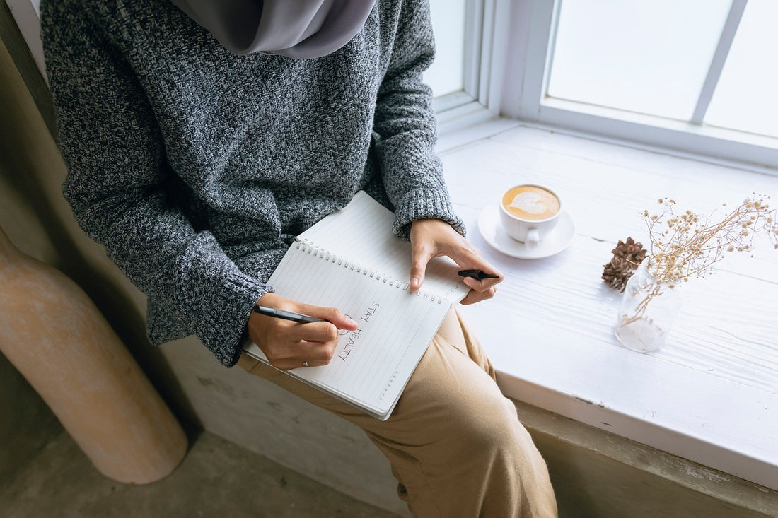 essential wellness being practice by person sitting next to a window with a self reflection journal, wellness by heart