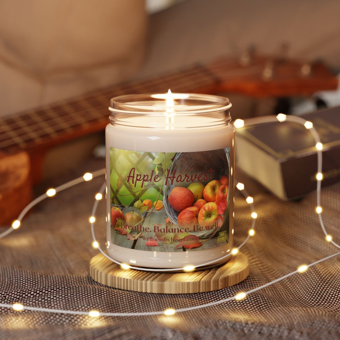 This candle is lit, sitting on a tablecloth with a guitar blurred in the background and fairy lights all around the table - wellness by heart